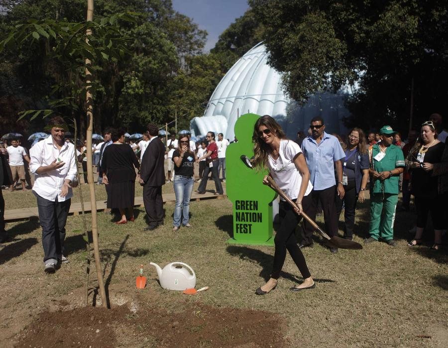 Gisele Bündchen planting a tree with a spade at the Green Nation Fest in Rio de Janeiro, surrounded by visitors