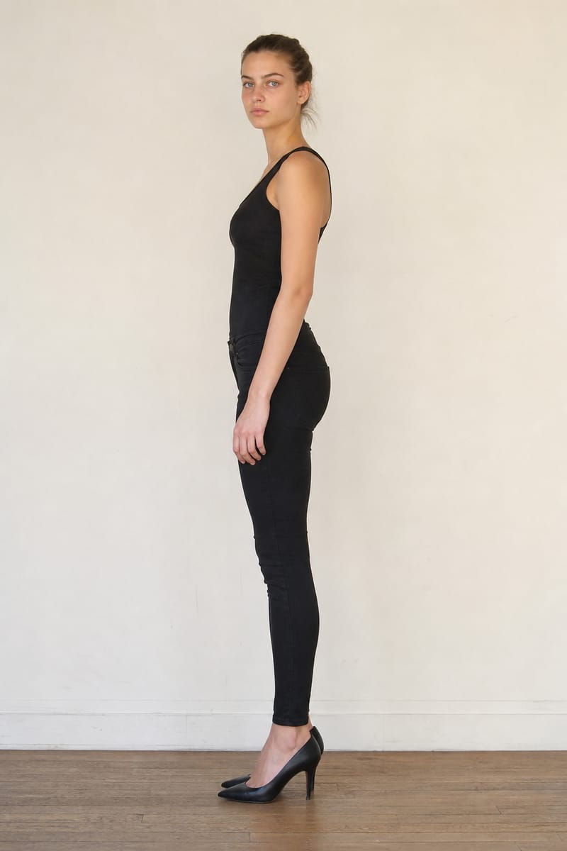Model digital in profile: plain black clothes, no make-up, against a light wall
