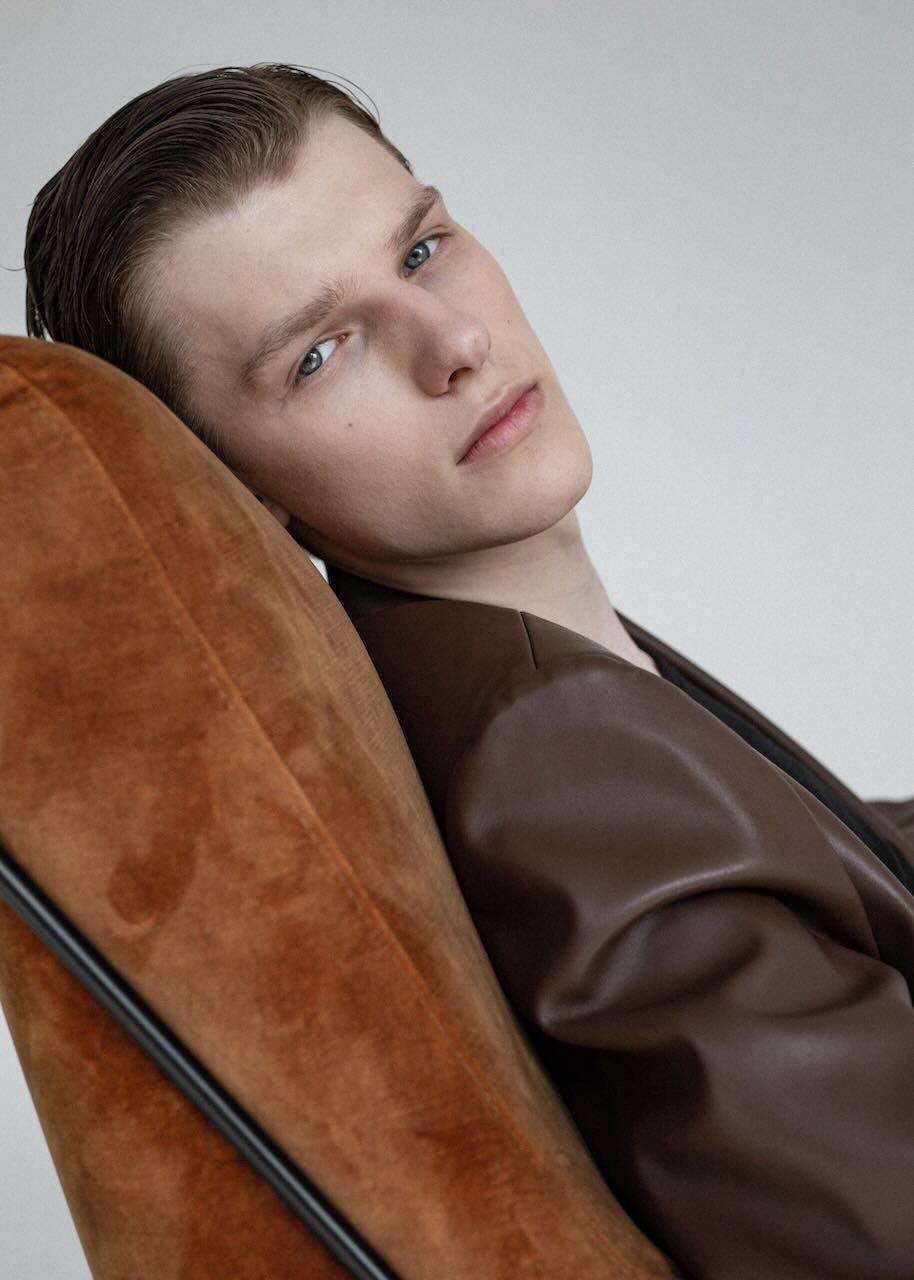Male model at a Supermodels shoot Young male model in a brown leather jacket leaning back in a chair in a studio