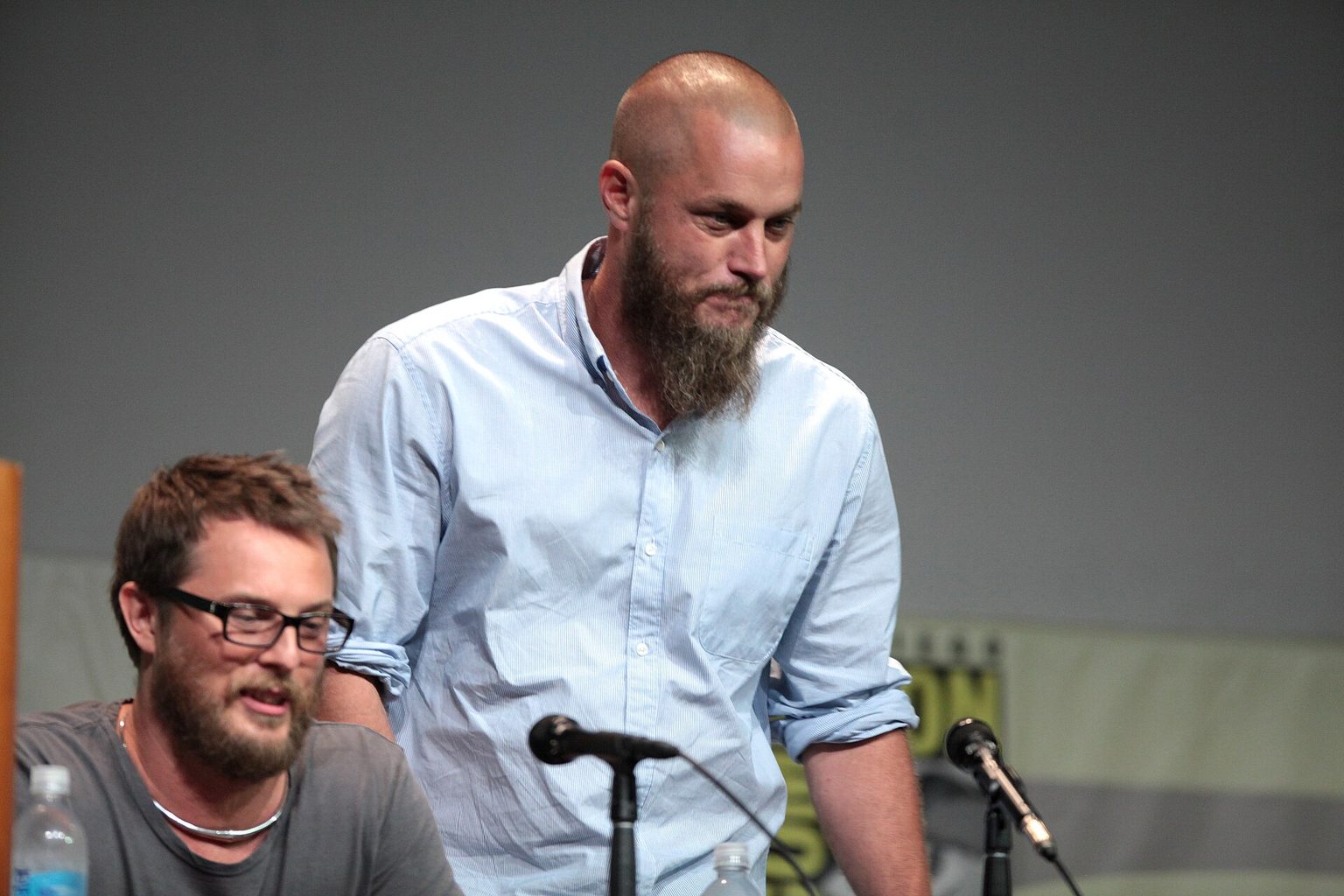 Travis Fimmel standing next to seated director Duncan Jones at a Comic-Con panel table